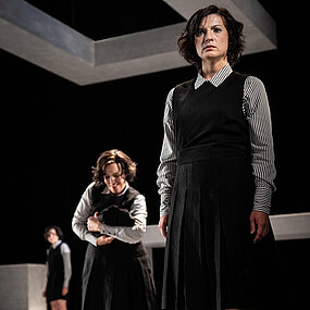 Mascha Kaléko (Katharina Shakina) steht vorne, schräg links hinter ihr einer weitere Mascha K. (Meret Engelhardt), die eine Jacke wie ein Baby hält, unscharf weiter hinten links ist eine weitere Mascha K. (Paulina Hobratschk).