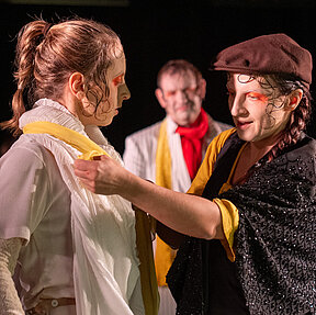 Caroline Frankenstein (Katharina Shakina) bindet Elisabeth Lavenza (Esther Berkel) ein gelbes Tuch um den Hals. Hinter ihnen Robert Walton (Paul Enev) und Alphonse Frankenstein (Klaas Schramm).