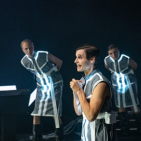 Konstantin Gries ist vorne und spricht lebhaft mit vor der Brust zusammengefalteten Händen. Spielende im Hintergrund beäugen ihn misstrauisch. 