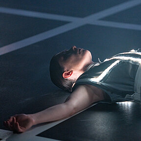 Tamara Theisen liegt auf dem weiß gerasterten Boden, die Arme seitlich ausgestreckt. 