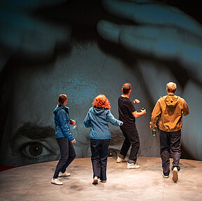 Die Freund:innen schrecken zurück vor einer großen Video-Projektion im Hintergrund der Bühne.