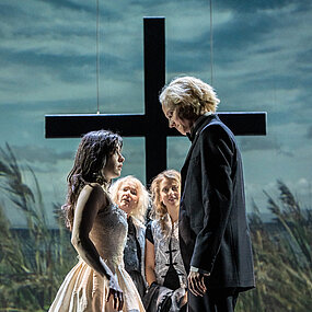 Elke (Tamara Theisen) und Hauke Haien (Tobias Schormann) schauen sich an, sie trägt ein Brautkleid. Hinter ihnen ein Kreuz und Schilfgras.