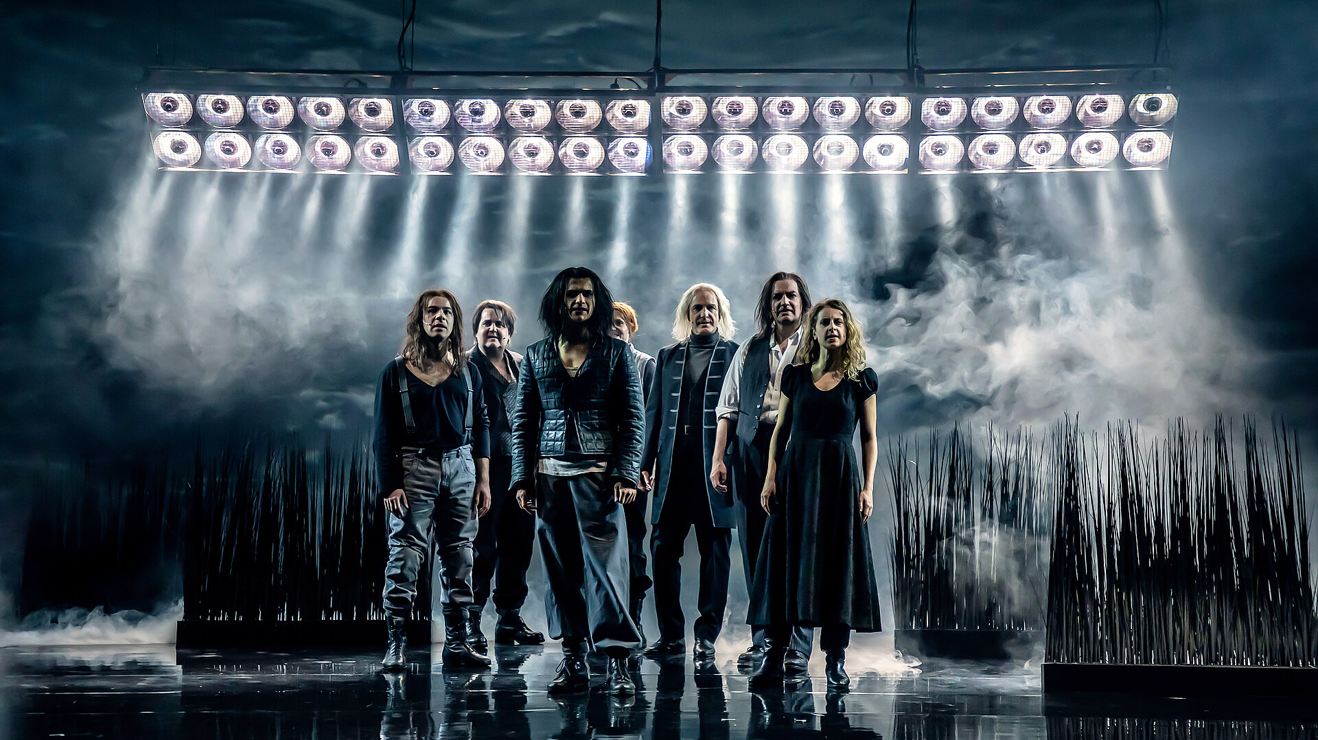 Die Dorfgemeinschaft als Chor. Im Hintergrund eine Graslandschaft und Scheinwerfer.