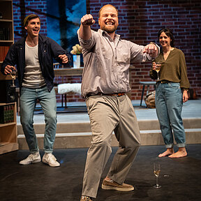 Julius (Florian Pelzer), Peer (Jan Wittje) und Luisa (Gesa Schierenstedt) in ausgelassener Stimmung. Julius und Luisa mit Weingläsern, Peer mimt Autofahren.