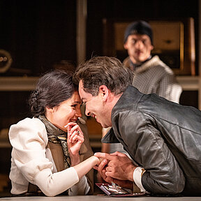 Nina Petersen (Paulina Hobratschk) und Jörgen (Darios Vaysi) Stirn an Stirn, sie lächeln sich verliebt an, Jörgen hält dabei Ninas Hand. Im Hintergrund beobachtet sie Carl Petersen (Florian Heise).